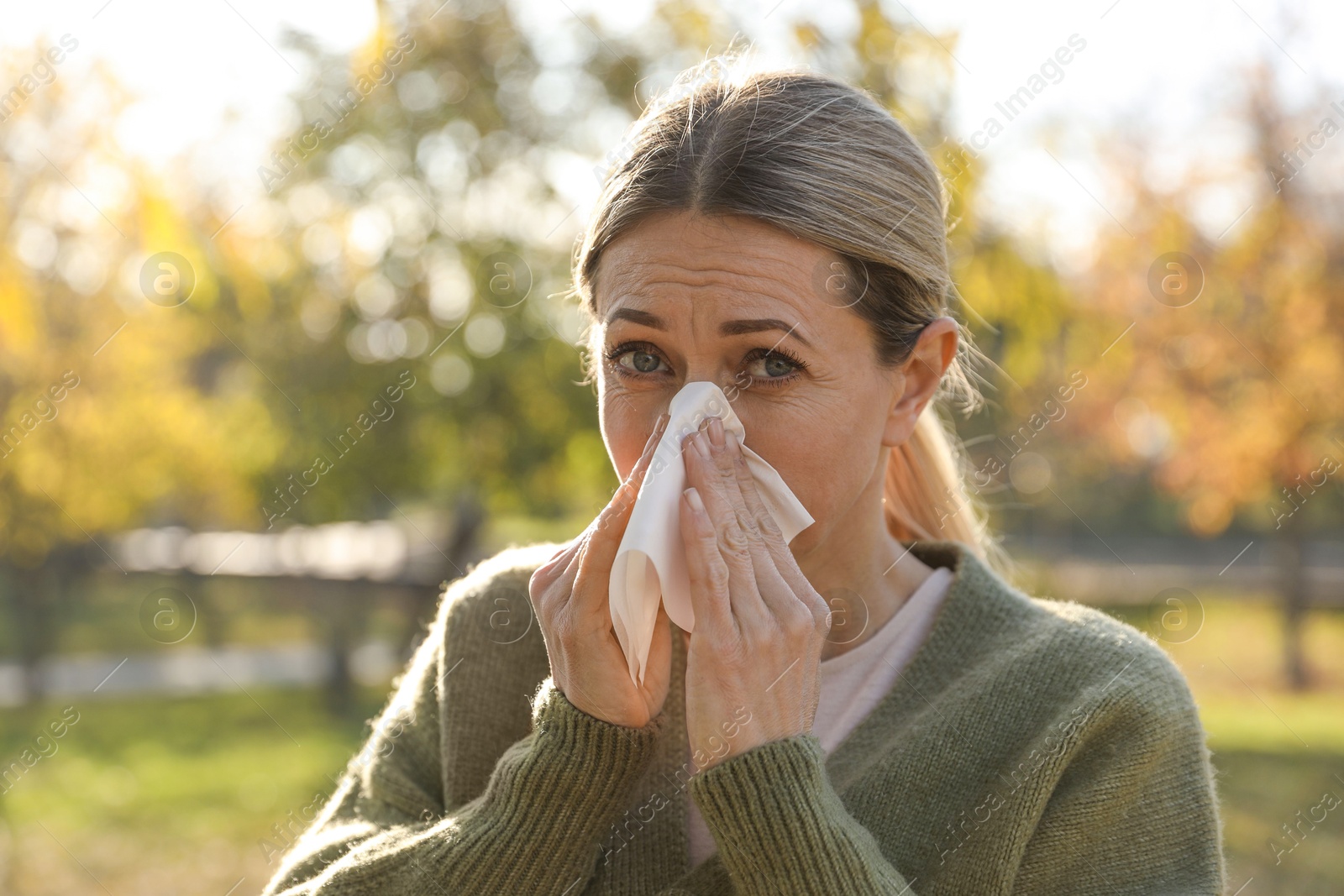 Photo of Woman with tissue blowing runny nose in park