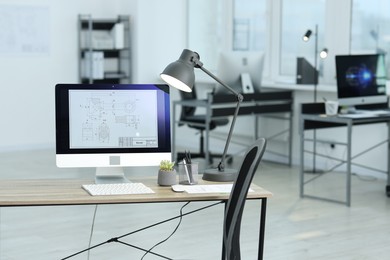 Photo of Computer with engineering drawing and lamp on desk in office