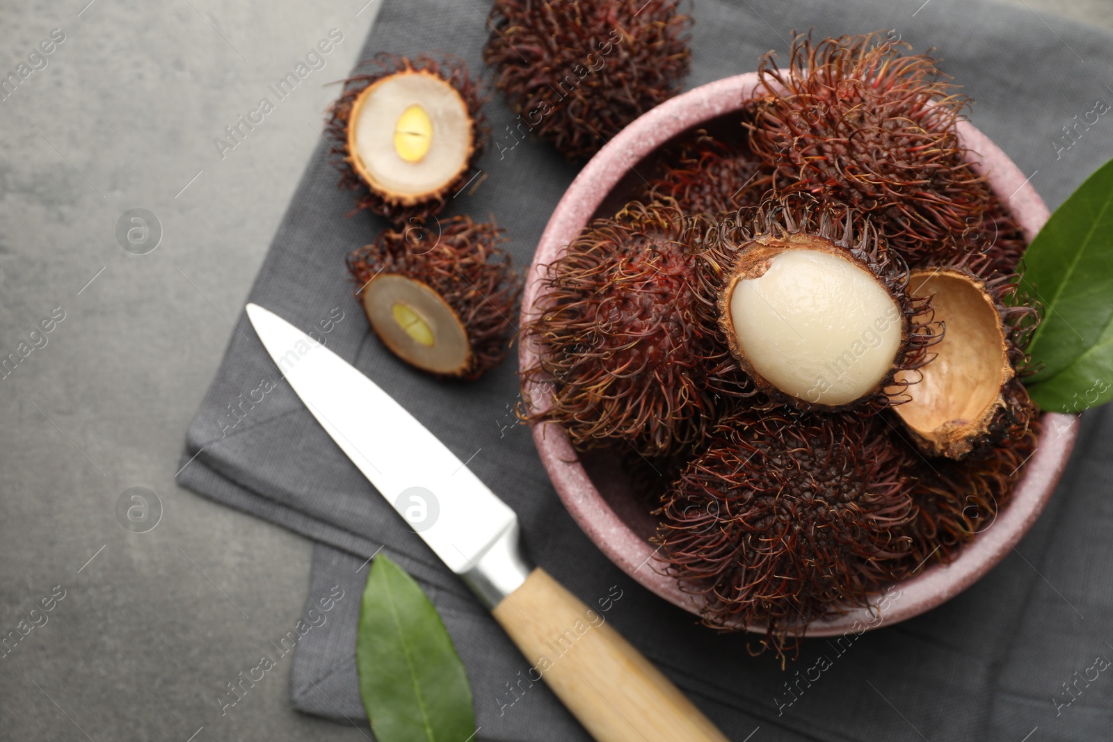 Photo of Delicious ripe rambutans, green leaves and knife on grey table, flat lay