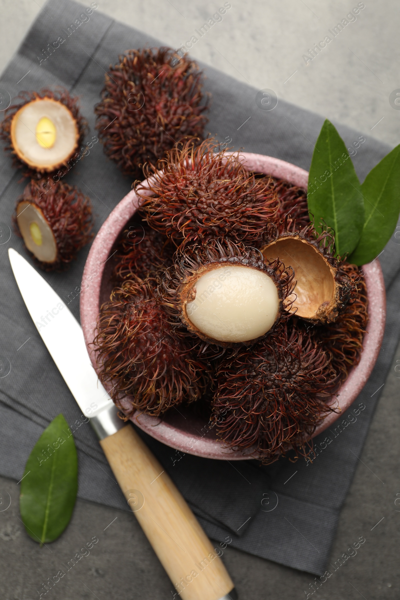 Photo of Delicious ripe rambutans, green leaves and knife on grey table, flat lay