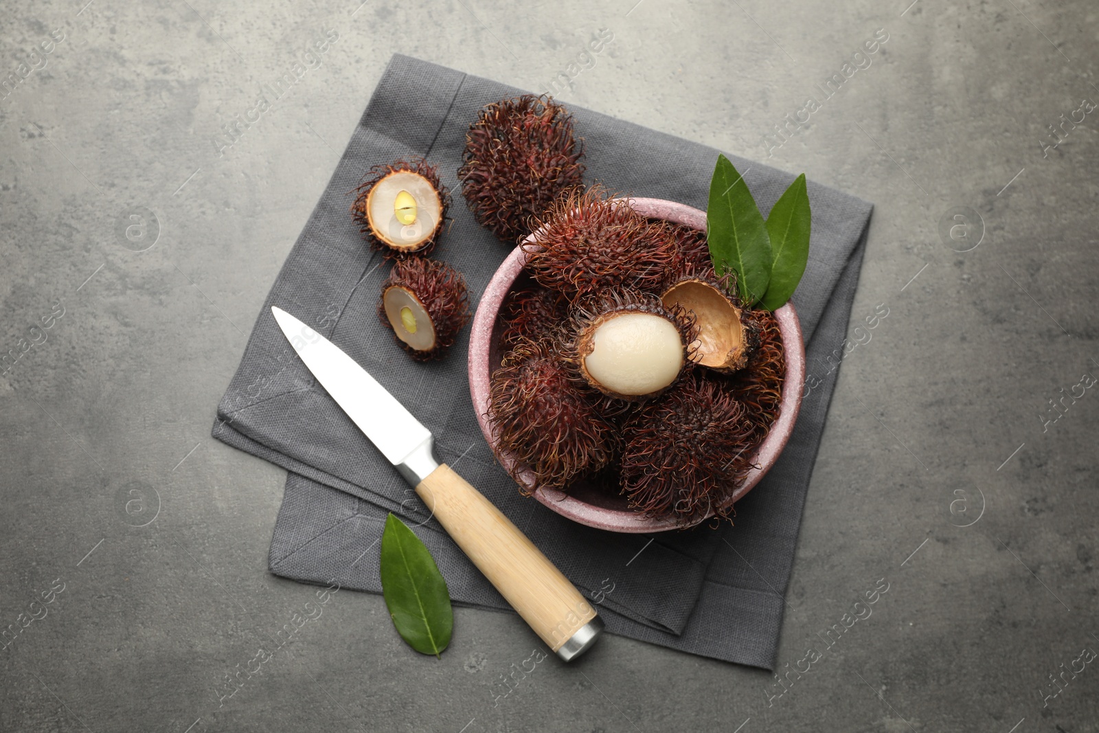 Photo of Delicious ripe rambutans, green leaves and knife on grey table, flat lay