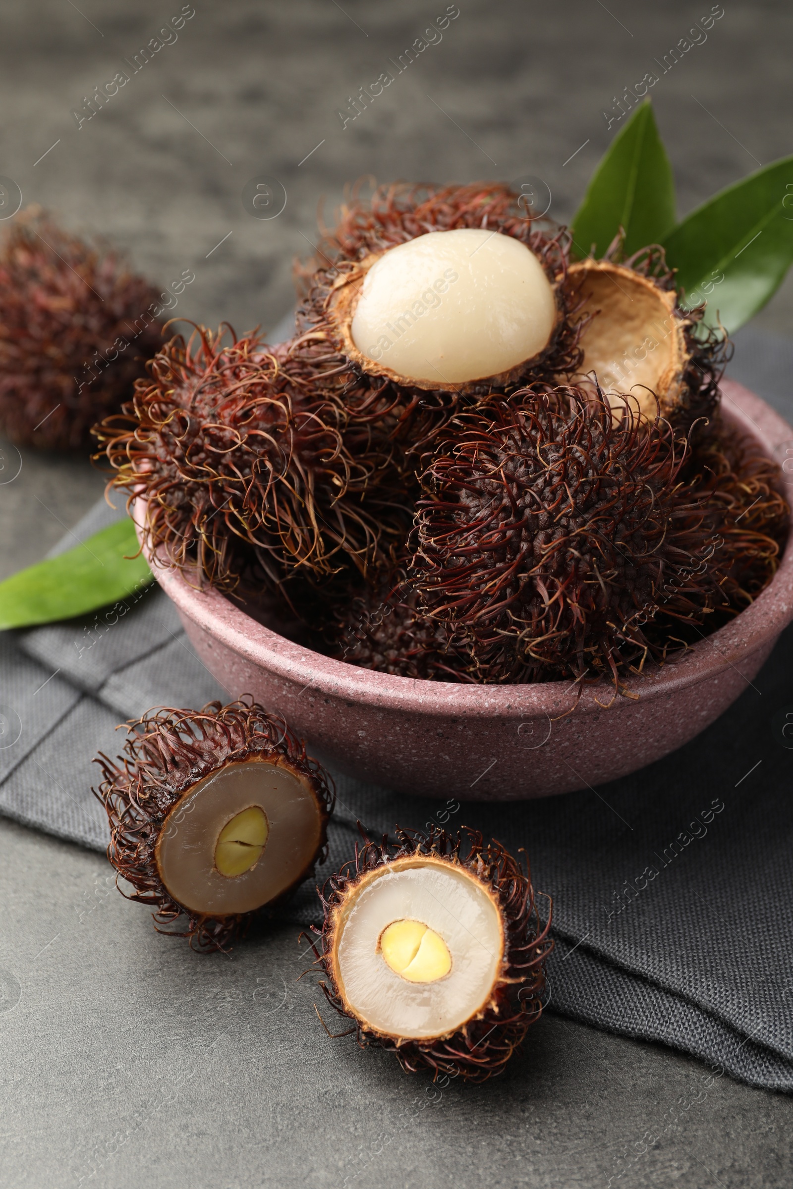 Photo of Delicious ripe rambutans and green leaves on grey table, closeup