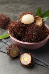 Photo of Delicious ripe rambutans and green leaves on grey table, closeup