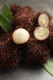 Photo of Delicious ripe rambutans and green leaves on grey table, closeup