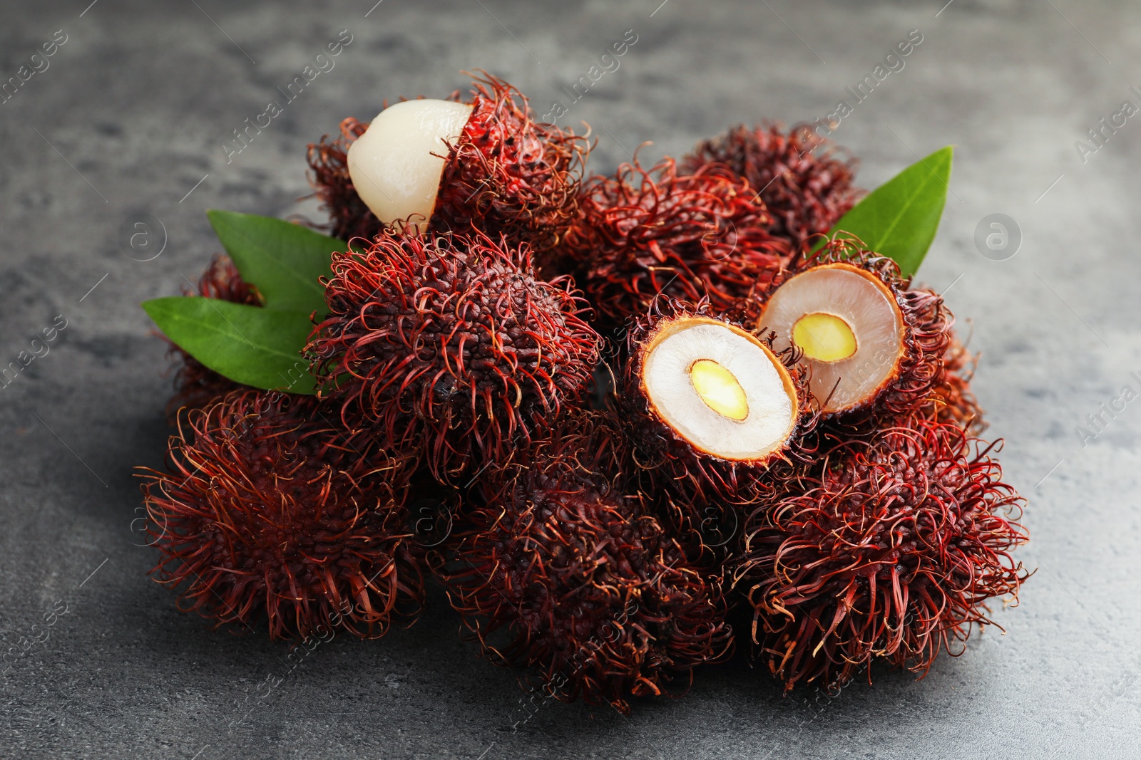 Photo of Delicious ripe rambutans and green leaves on grey table, closeup