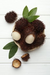 Delicious ripe rambutans and green leaves on white wooden table, top view