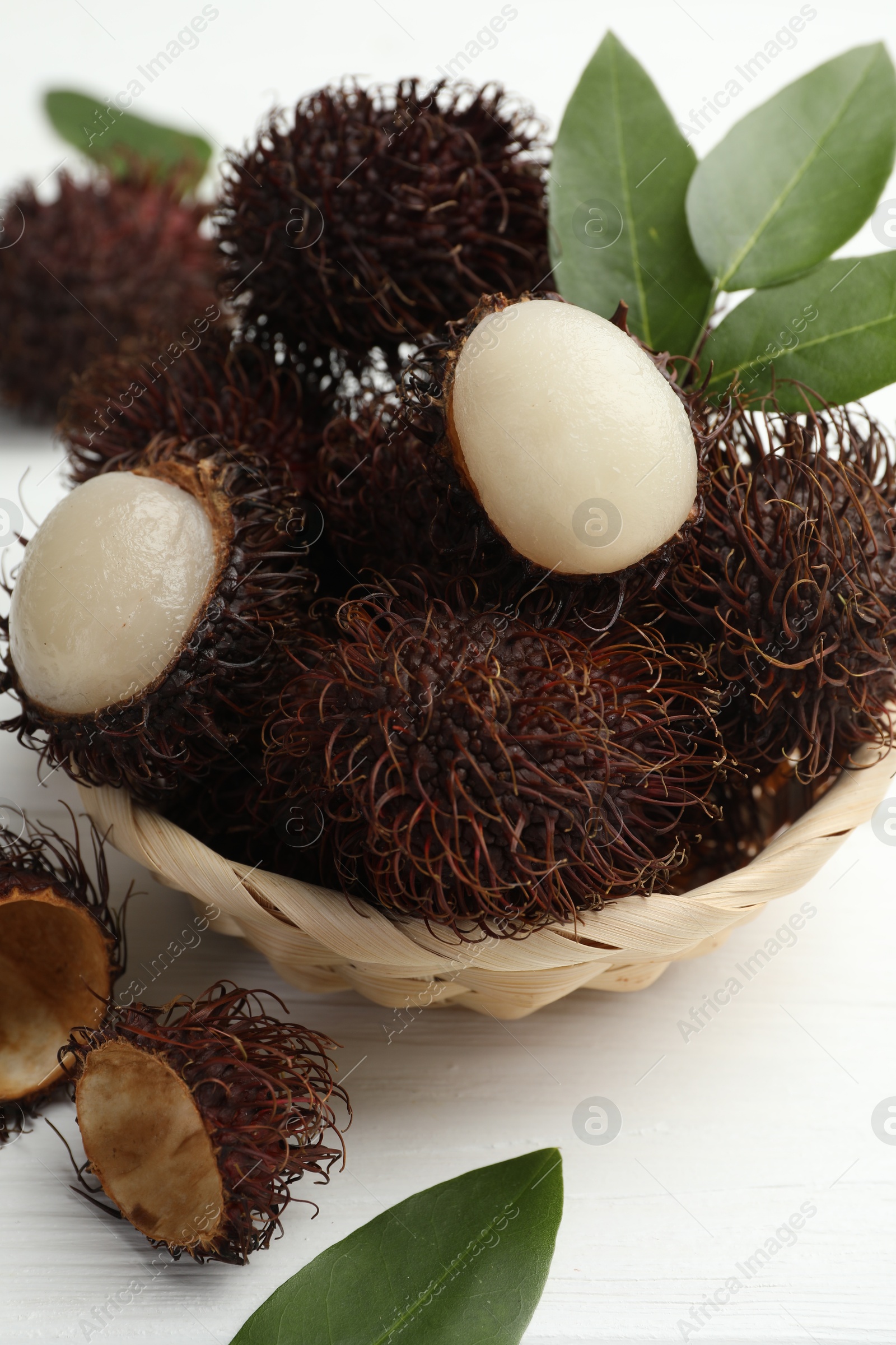 Photo of Delicious ripe rambutans and green leaves on white wooden table, closeup