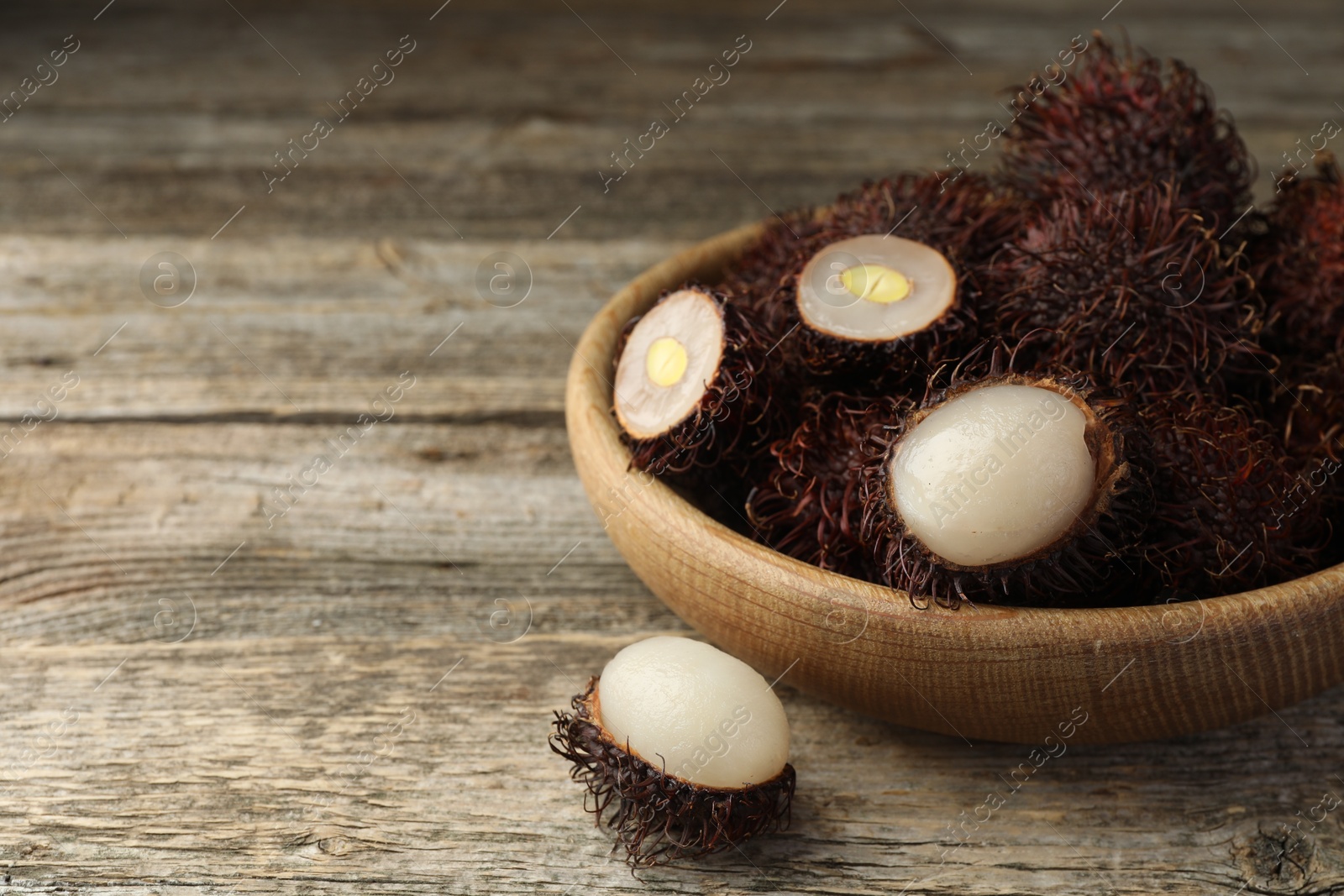 Photo of Delicious ripe rambutans on wooden table, closeup. Space for text