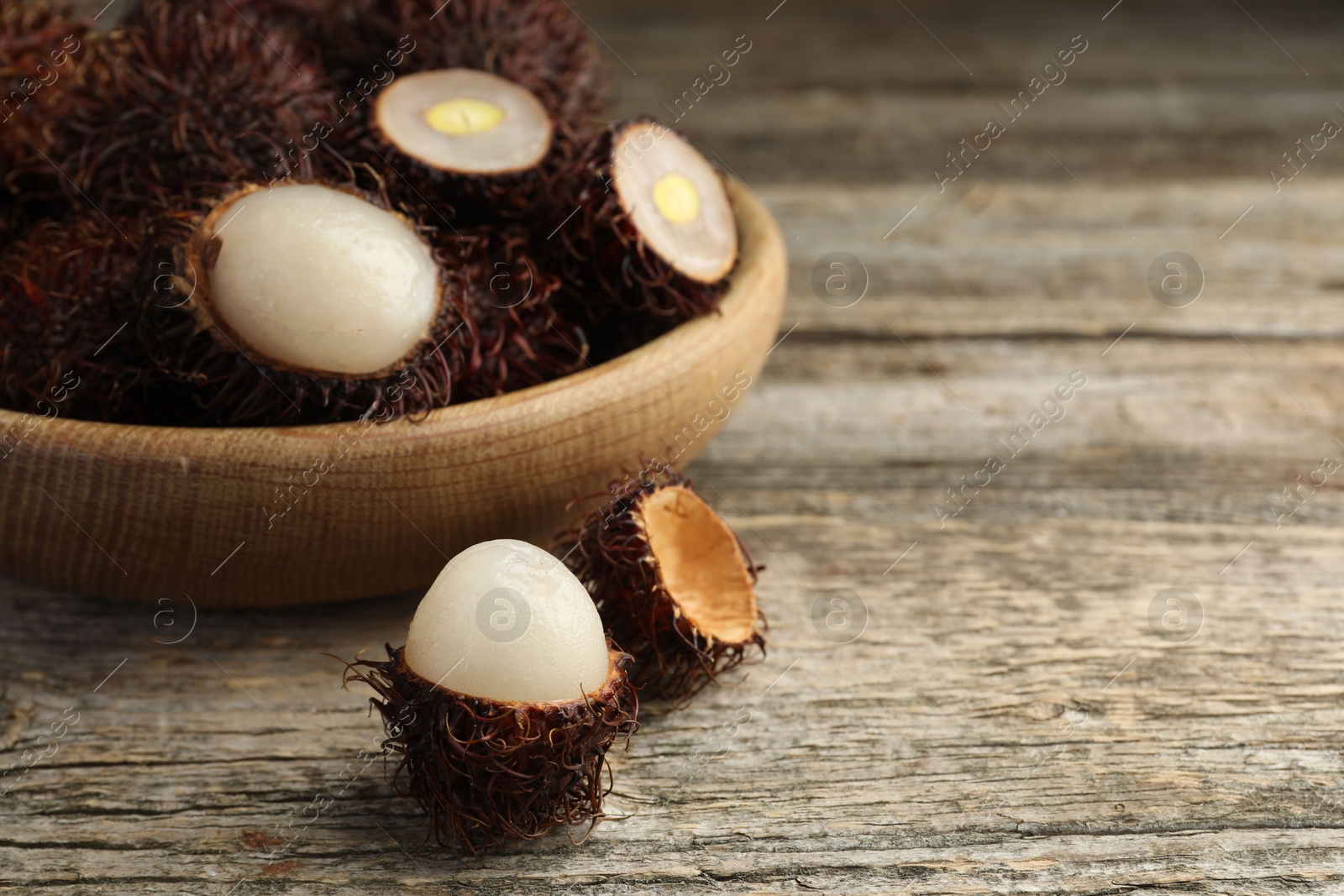 Photo of Delicious ripe rambutans on wooden table, closeup. Space for text