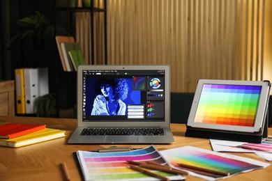 Photo of Designer's workplace with laptop, tablet, stationery and palettes on wooden table indoors