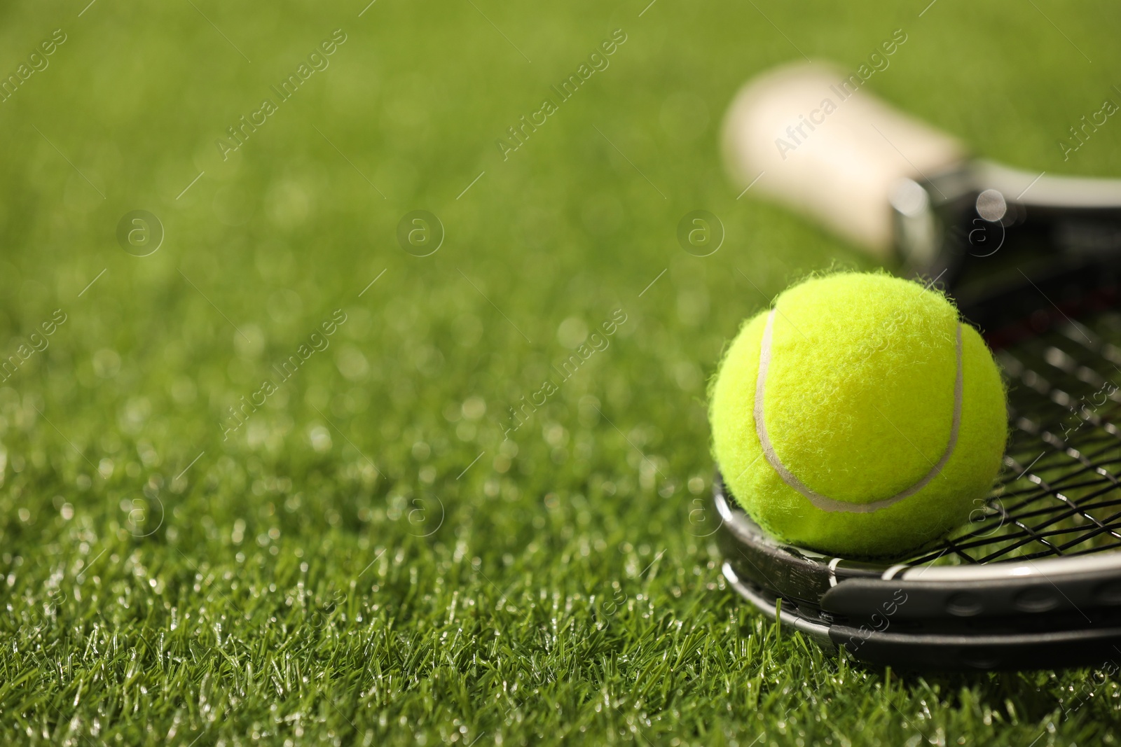 Photo of Tennis racket and ball on green artificial grass, closeup. Space for text