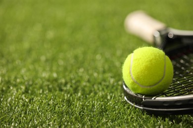 Photo of Tennis racket and ball on green artificial grass, closeup. Space for text