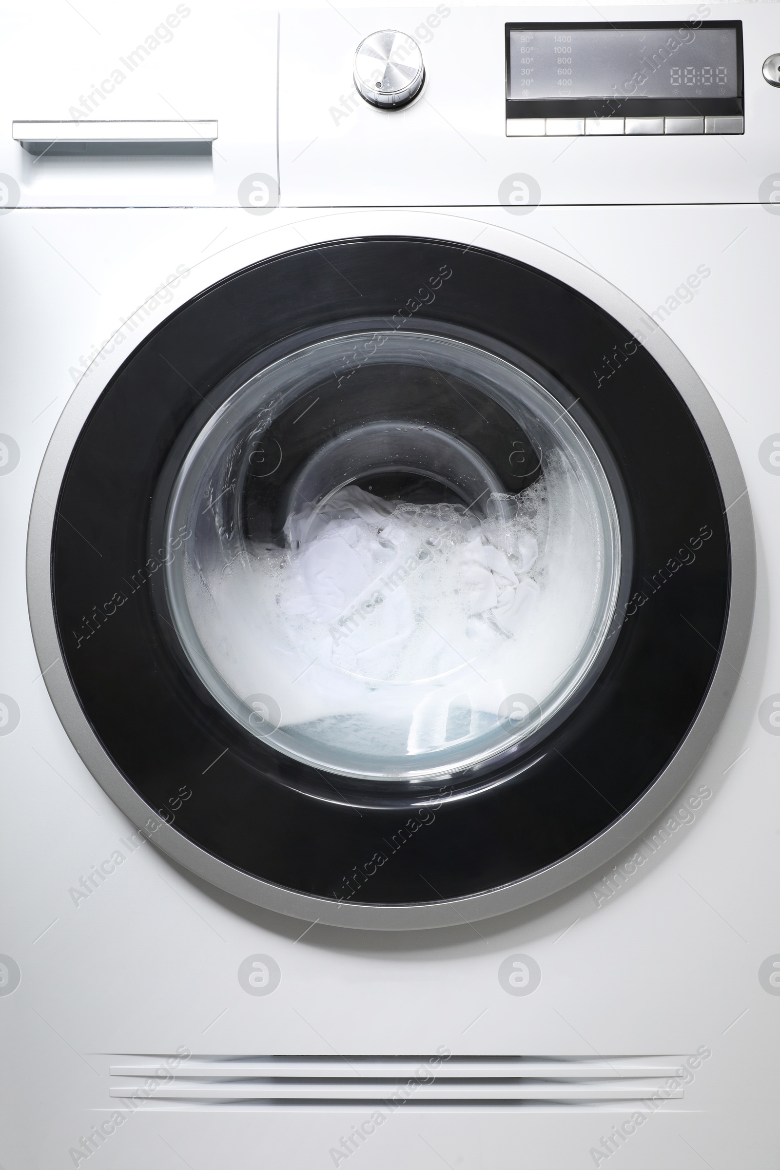 Photo of Washing machine with clothes and suds as background, closeup