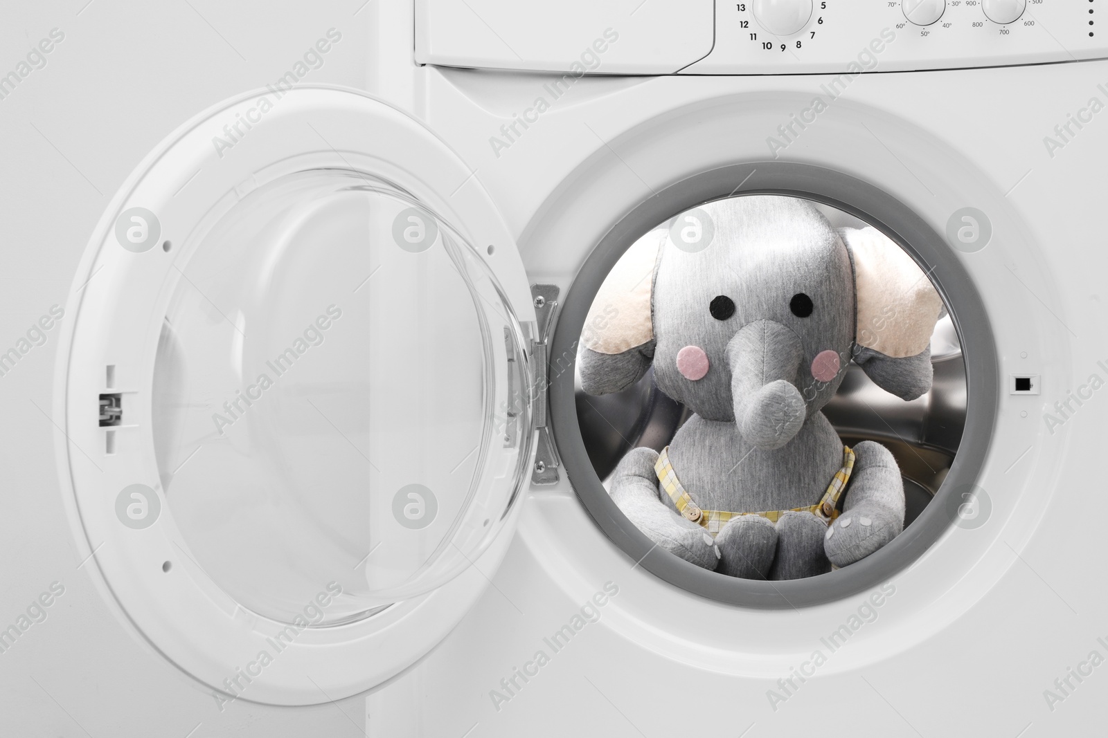 Photo of Washing machine with toy elephant near light wall, closeup