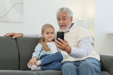 Photo of Grandpa and his granddaughter watching something on smartphone at home