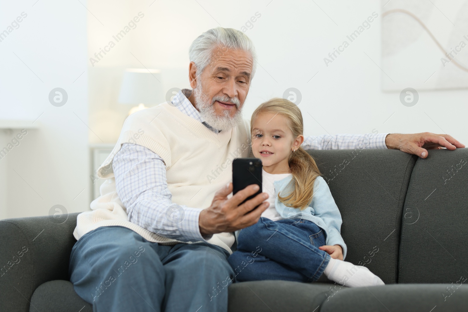 Photo of Grandpa and his granddaughter watching something on smartphone at home