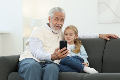 Photo of Grandpa and his granddaughter watching something on smartphone at home