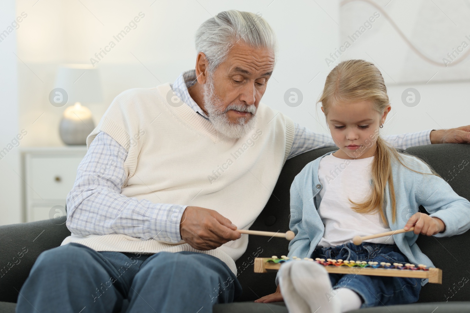 Photo of Grandpa and his granddaughter playing toy xylophone on sofa at home