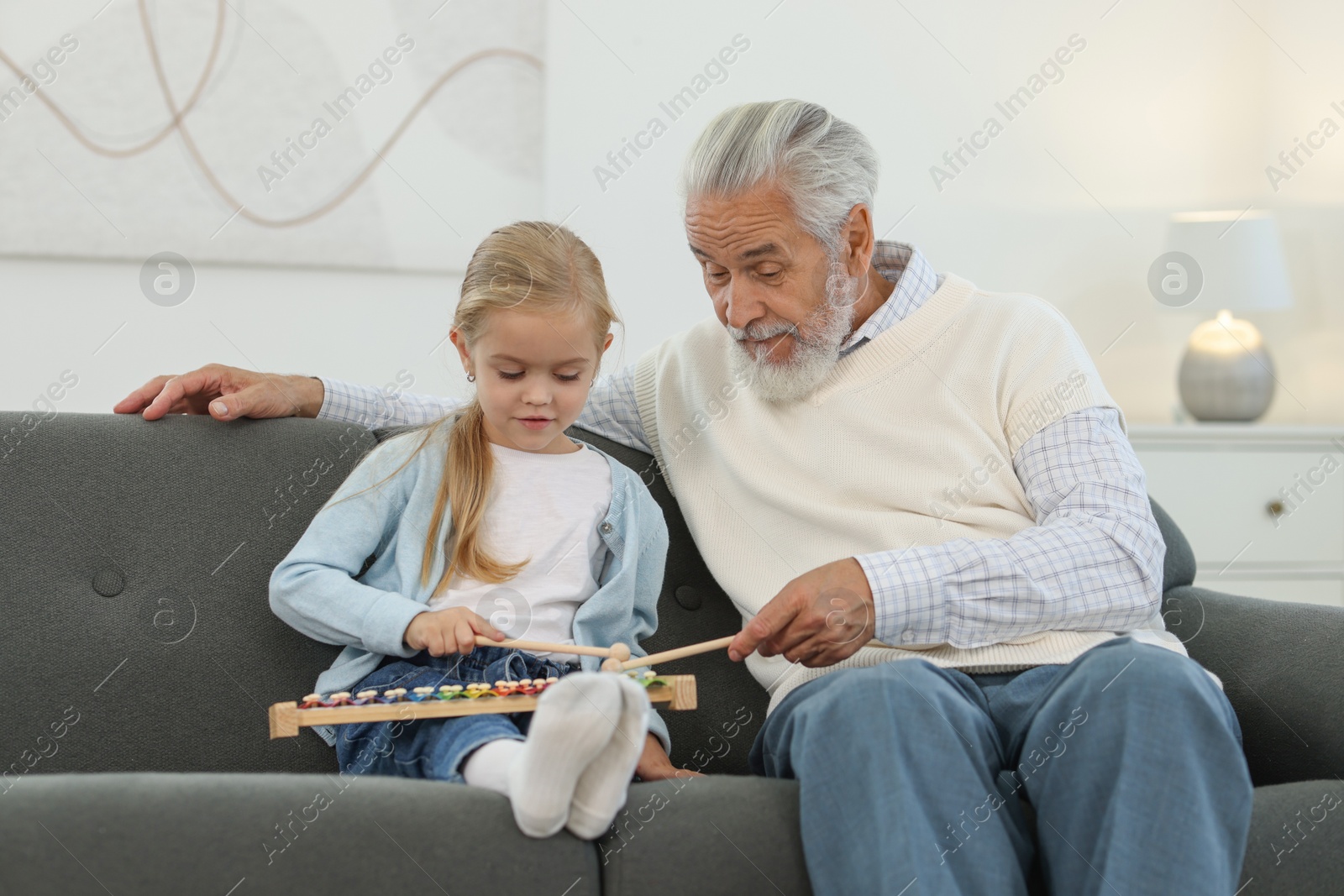 Photo of Grandpa and his granddaughter playing toy xylophone on sofa at home