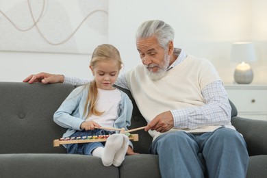 Photo of Grandpa and his granddaughter playing toy xylophone on sofa at home