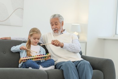 Photo of Grandpa and his granddaughter playing toy xylophone on sofa at home