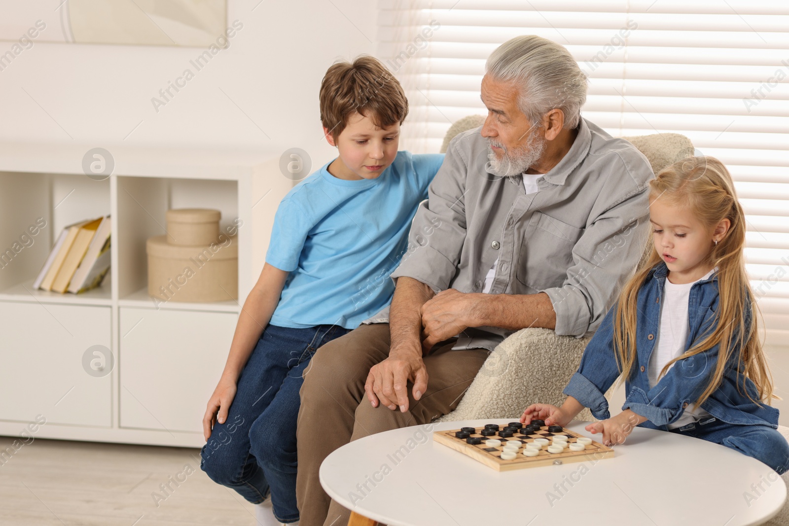 Photo of Grandpa and his grandkids playing checkers at table indoors