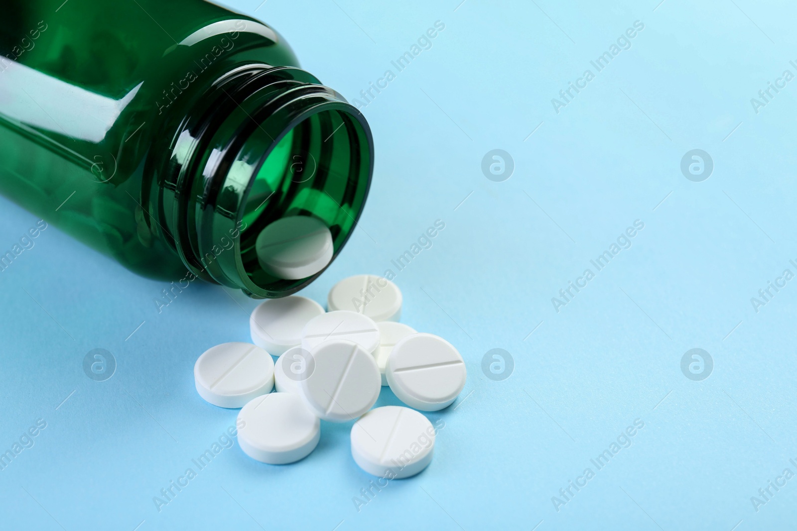 Photo of Medical bottle with antibiotic pills on light blue background, closeup. Space for text