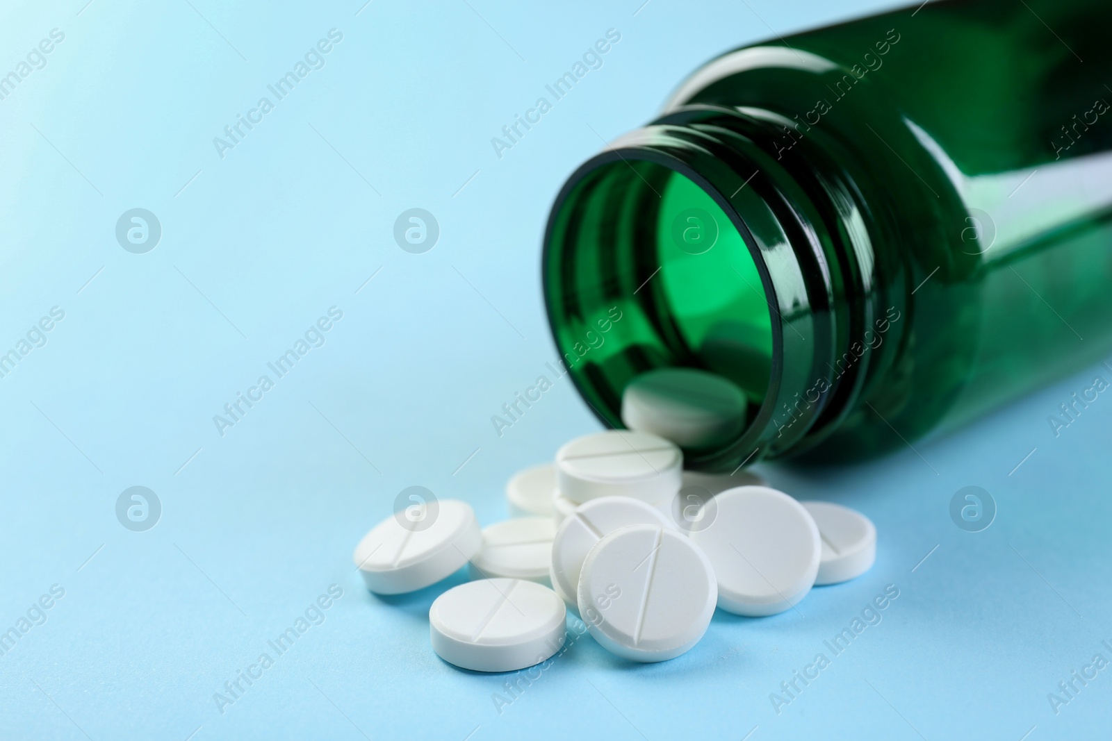 Photo of Medical bottle with antibiotic pills on light blue background, closeup. Space for text