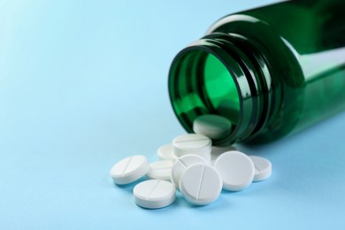 Photo of Medical bottle with antibiotic pills on light blue background, closeup. Space for text