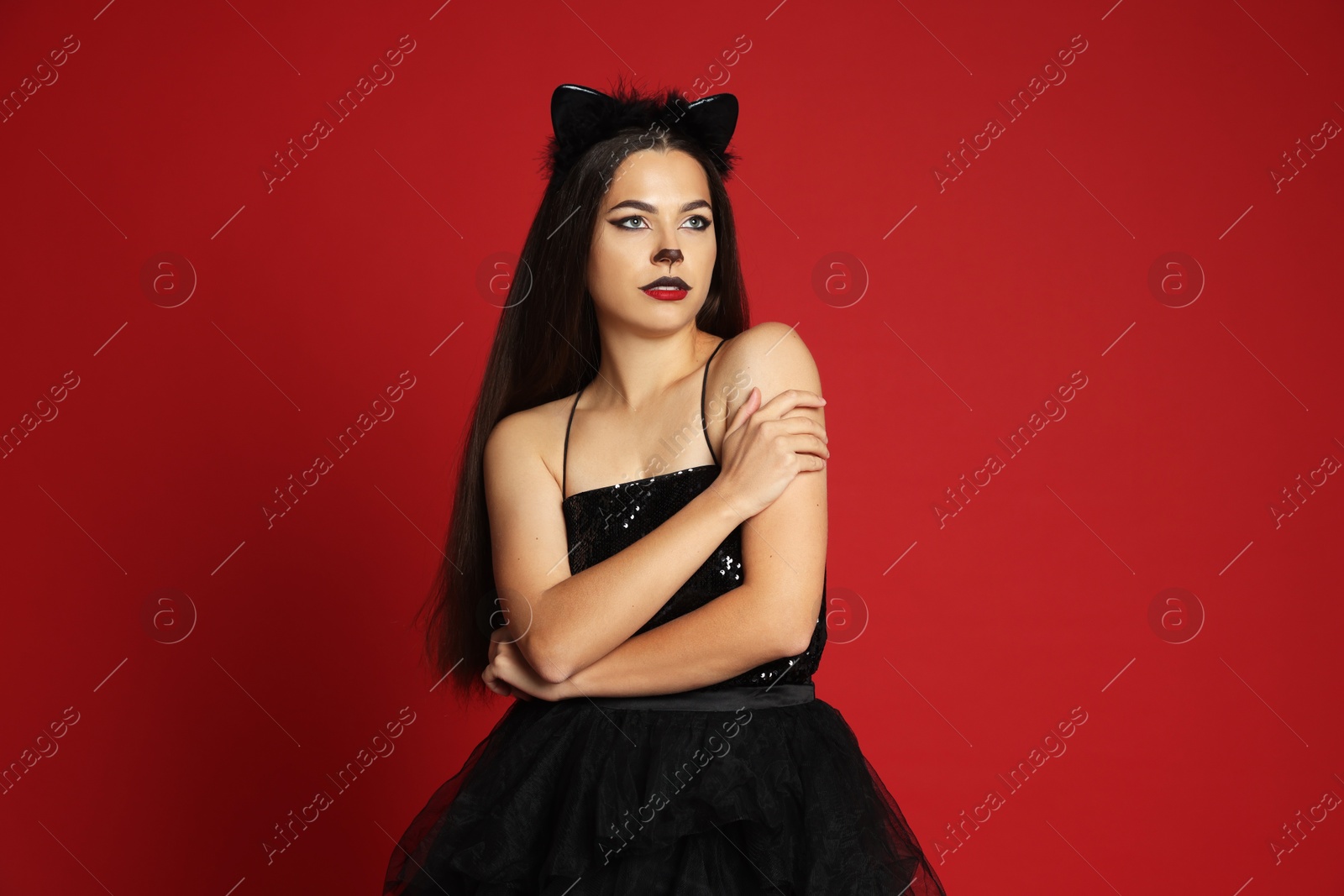 Photo of Woman with cat makeup and ears in beautiful dress on red background