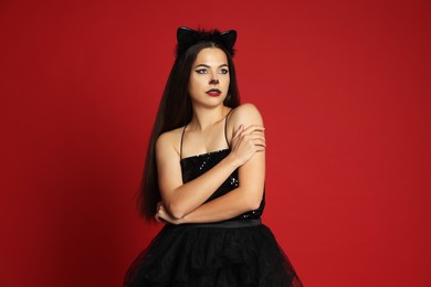 Photo of Woman with cat makeup and ears in beautiful dress on red background