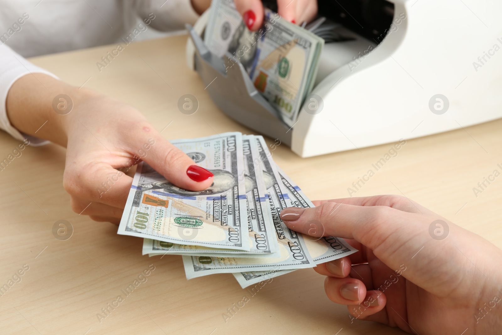 Photo of Cashier giving dollar banknotes to client at table in money exchange, closeup