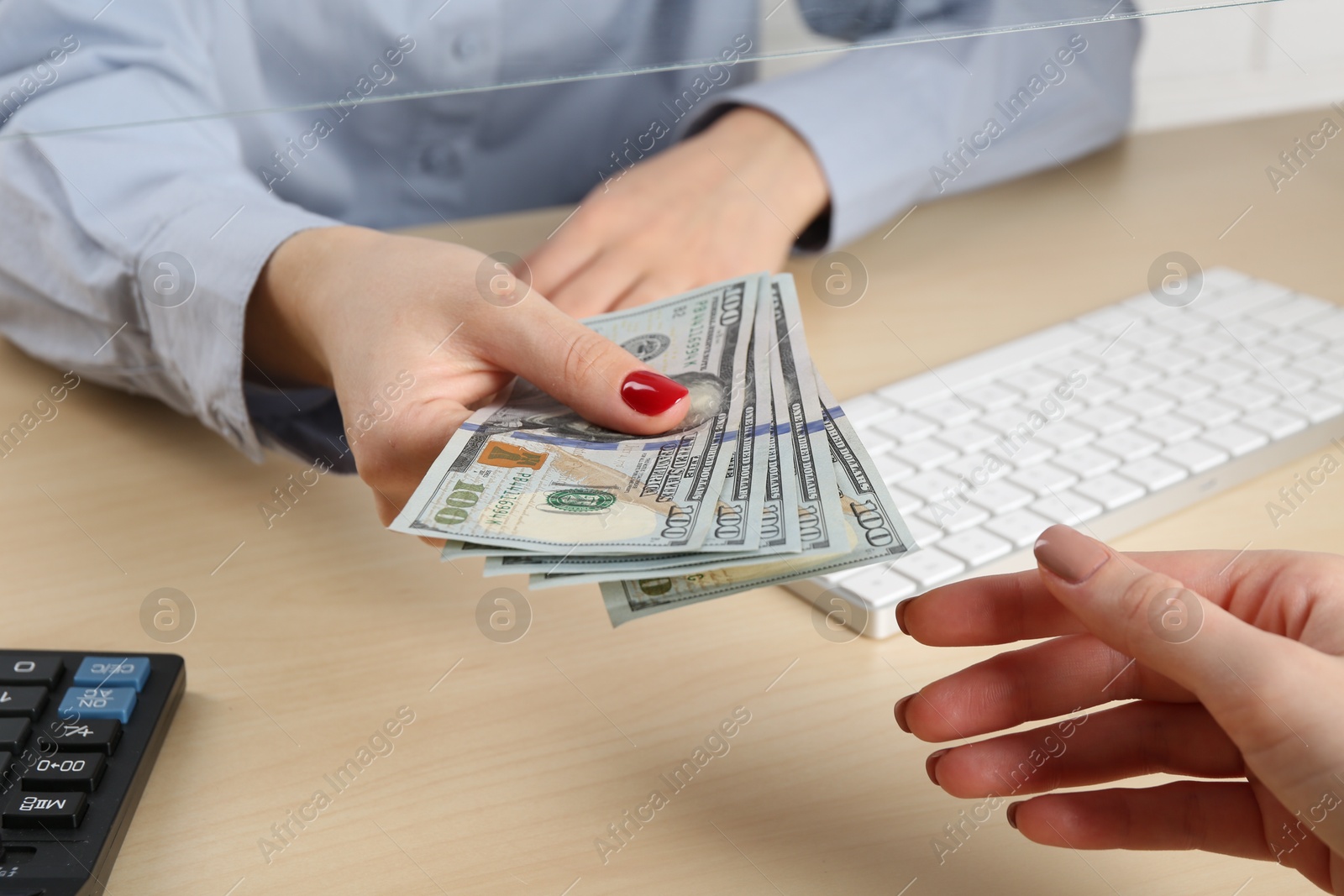 Photo of Cashier giving dollar banknotes to client at table in money exchange, closeup