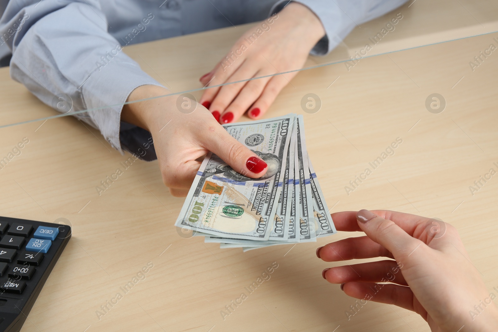 Photo of Cashier giving dollar banknotes to client at table in money exchange, closeup