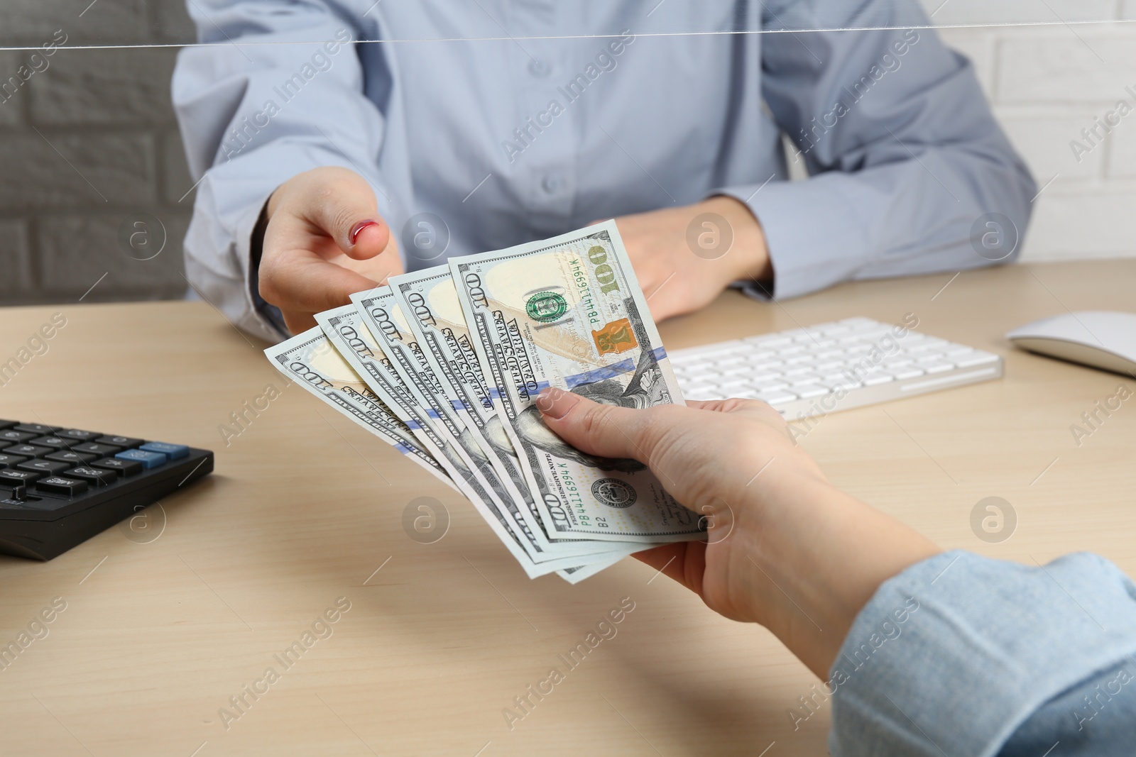 Photo of Client giving dollar banknotes to cashier at table in money exchange, closeup