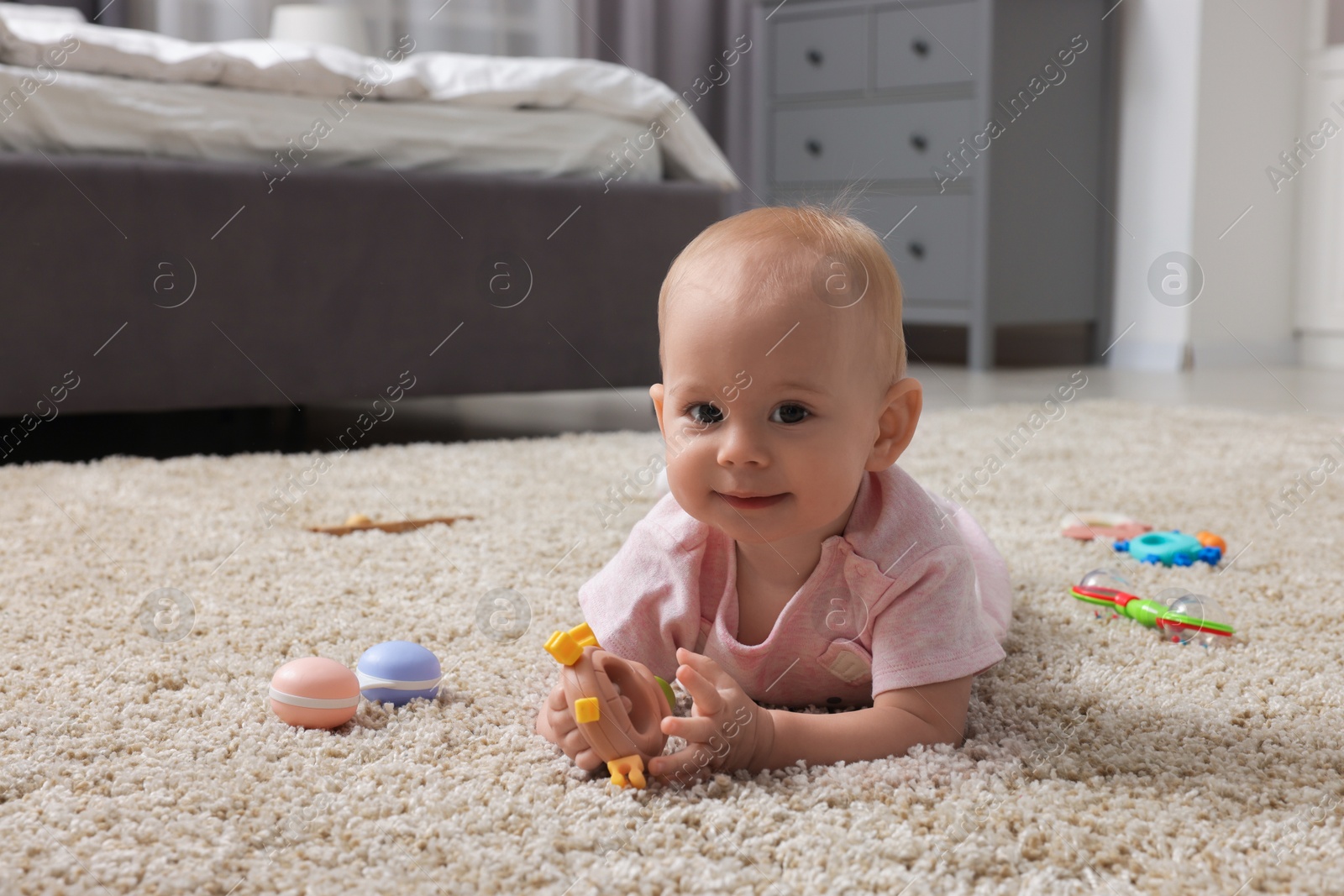 Photo of Cute little baby with rattles on floor indoors