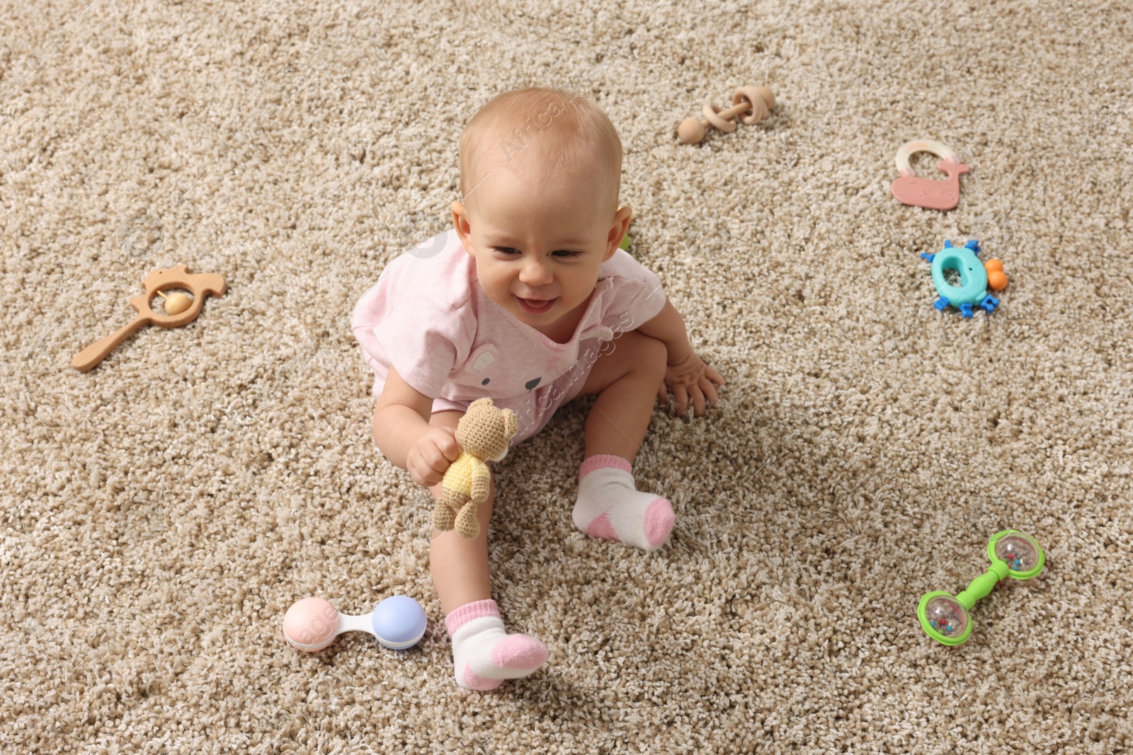 Photo of Cute little baby with rattles on floor indoors