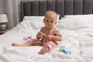 Photo of Cute little baby with rattles on bed indoors