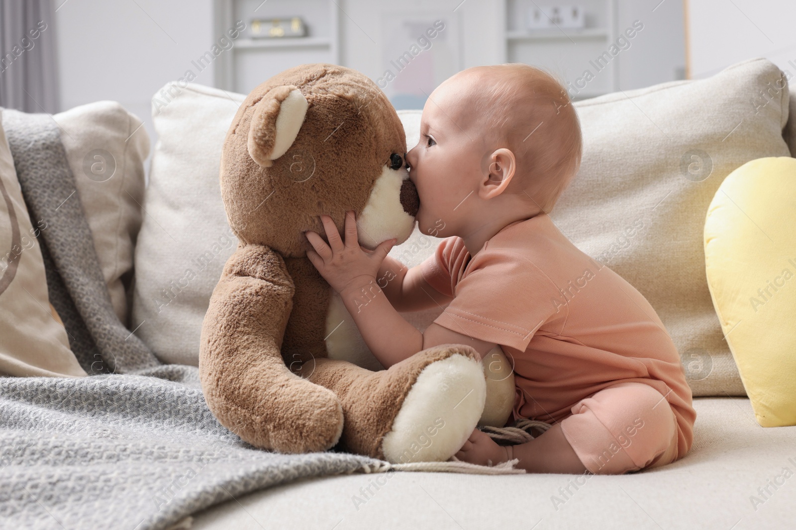 Photo of Cute little baby with teddy bear on sofa indoors