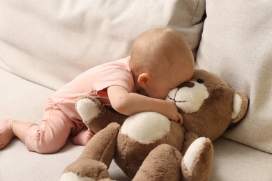 Photo of Cute little baby with teddy bear on sofa indoors