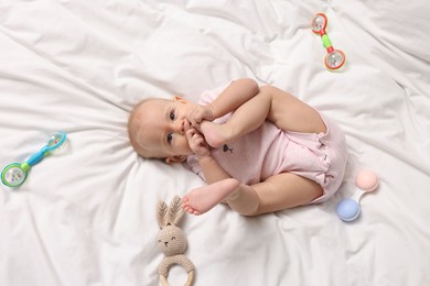 Photo of Cute little baby with rattles on bed indoors, top view