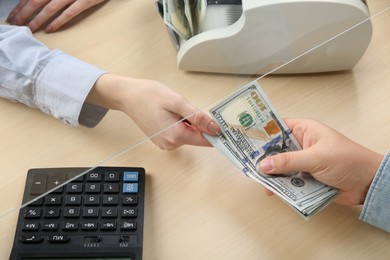 Photo of Client giving dollar banknotes to cashier at table in money exchange, closeup