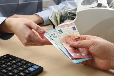 Photo of Client giving euro banknotes to cashier at table in money exchange, closeup