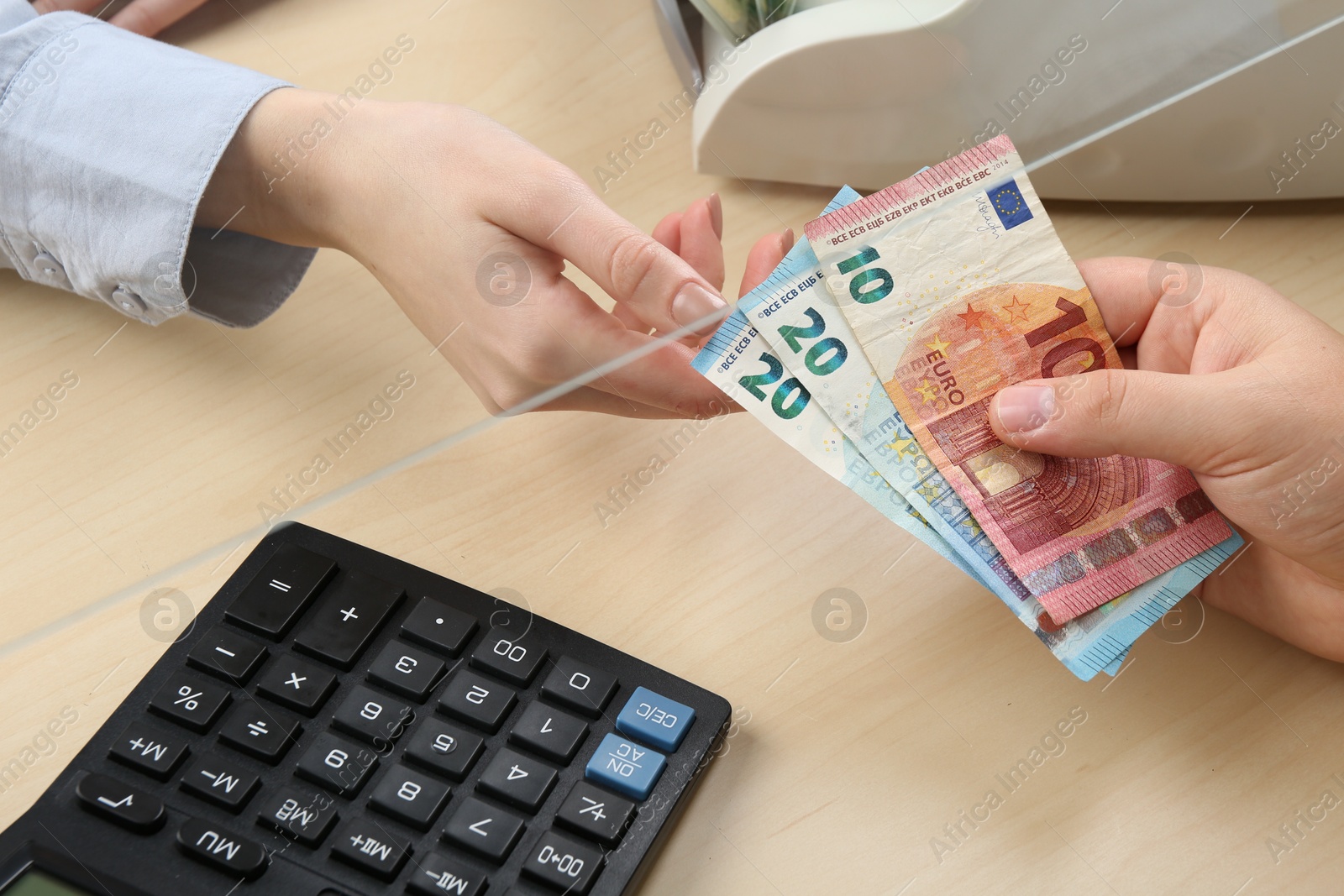 Photo of Client giving euro banknotes to cashier at table in money exchange, closeup