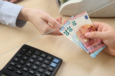 Photo of Client giving euro banknotes to cashier at table in money exchange, closeup