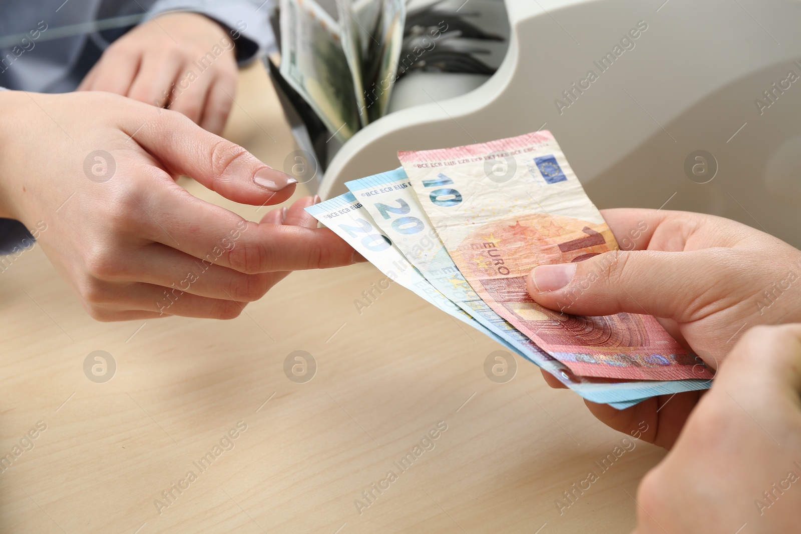 Photo of Client giving euro banknotes to cashier at table in money exchange, closeup