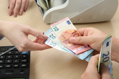 Photo of Client giving euro banknotes to cashier at table in money exchange, closeup