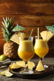 Photo of Tasty pineapple cocktail in glasses served on wooden table