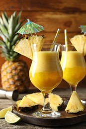 Photo of Tasty pineapple cocktail in glasses served on wooden table