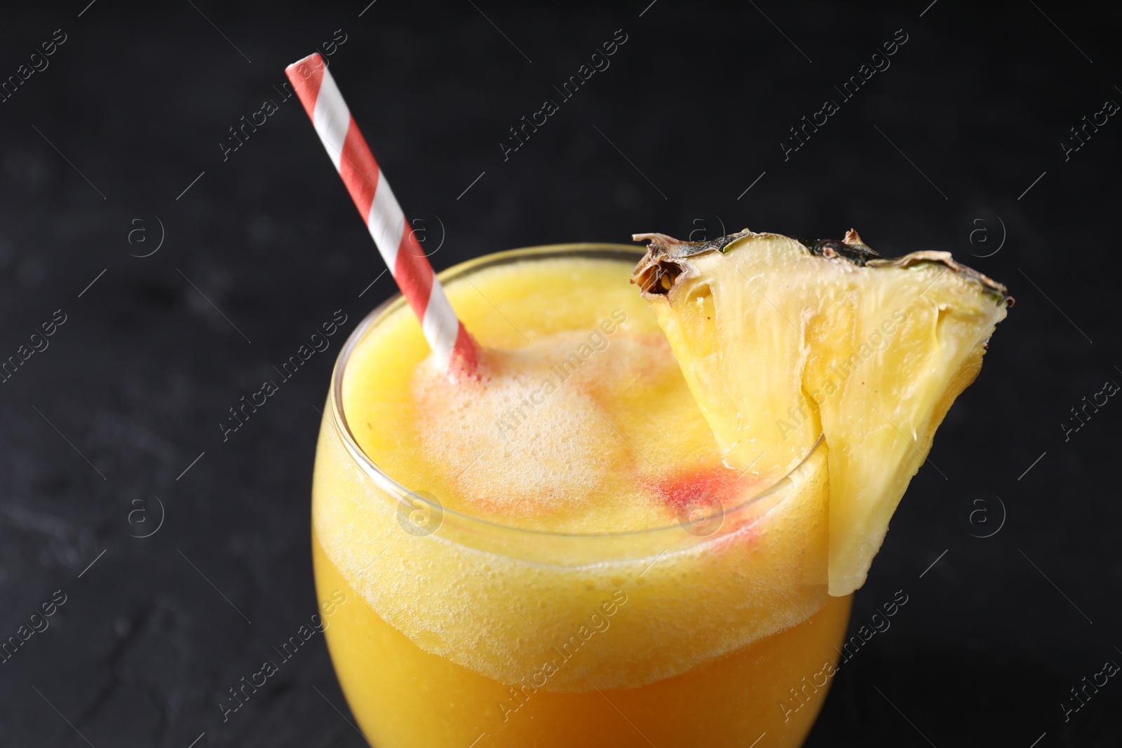 Photo of Tasty pineapple cocktail in glass served on black table, closeup